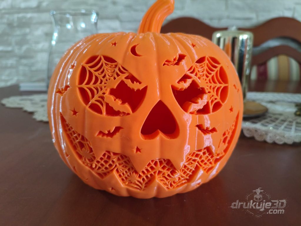 Pomarańczowa dynia z druku 3D o szerokości 24 cm, z ażurową twarzą wypełnioną pajęczynami, nietoperzami i gwiazdkami