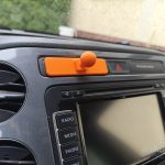 Pomarańczowe mocowanie telefonu do kokpitu z druku 3D wpięte w szczelinę nad radiem w desce rozdzielczej Volkswagena