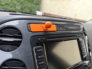 Pomarańczowe mocowanie telefonu do kokpitu z druku 3D wpięte w szczelinę nad radiem w desce rozdzielczej Volkswagena